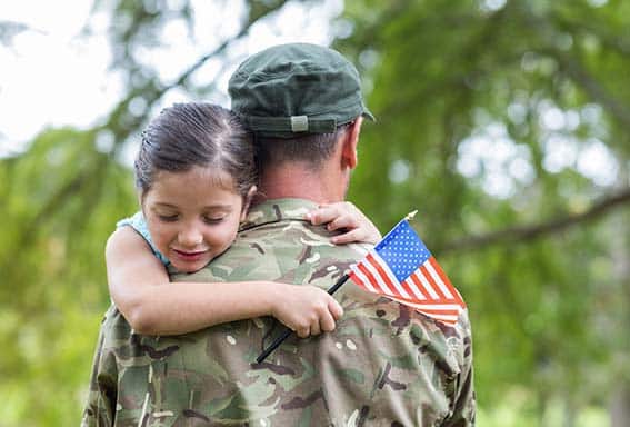 veteran father holds young daughter in his arms.